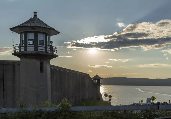 A guard tower and wall at the Sing Sing prison overlook a river at sunset.